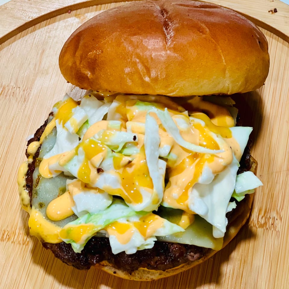 A close-up of a burger with melted cheese, shredded lettuce, and orange sauce on a wooden board.