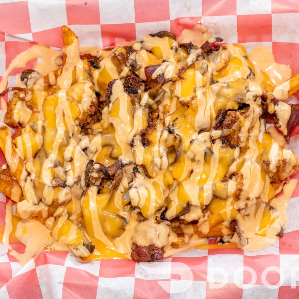 Cheesy fries topped with steak and a creamy sauce, served in a red and white checkered paper.