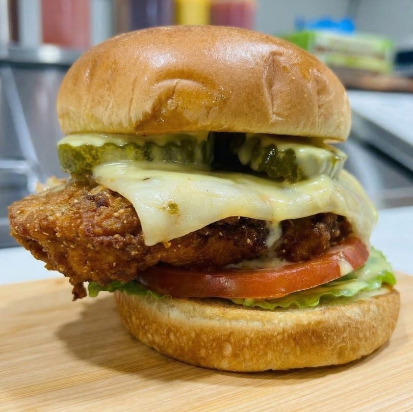 A crispy fried chicken sandwich with melted cheese, pickles, tomato, and lettuce on a bun.