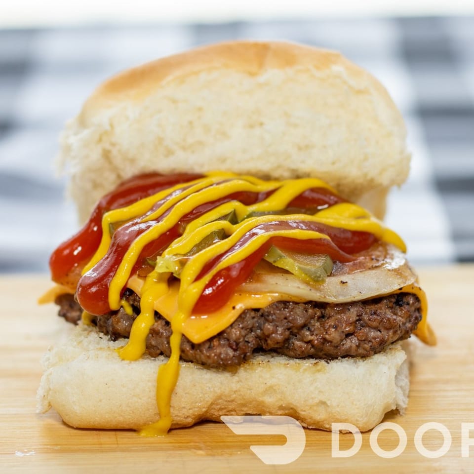 Cheeseburger with melted cheese, pickles, onions, ketchup, and mustard on a bun.